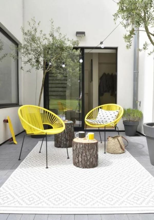 Terrasse dekorieren mit weißem Outdoor Teppich und Baumstümpfen als Beistelltische
