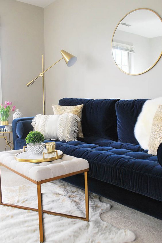 Goldene Akzente im Interieur gemütliches Wohnzimmer marineblaue Couch Stehlampe Tisch Wandspiegel weiße Kissen