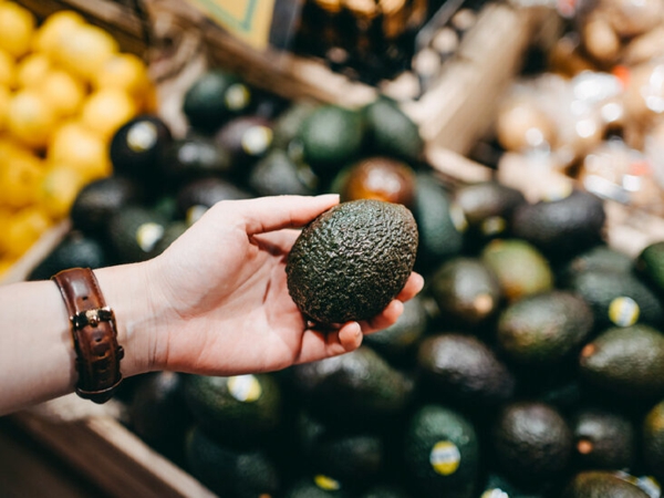 Woman shopping for fresh fruit and vegetables in supermarket, close up of her hand choosing avocados