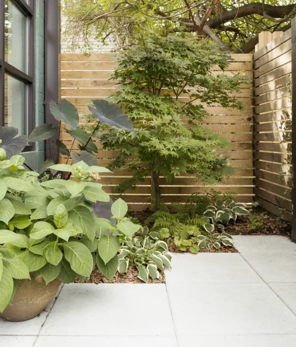Sichtschutz Ideen im Garten hoher Zaun aus Holz grüne Pflanzen graue Platten auf dem Boden 