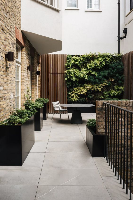 minimalistische Terrassengestaltung kleine Terrasse in der Stadt zwischen Häusern minimalistisch gestaltet großformatige Bodenfliesen hohe Pflanzkübel runder Tisch Metallstuhl