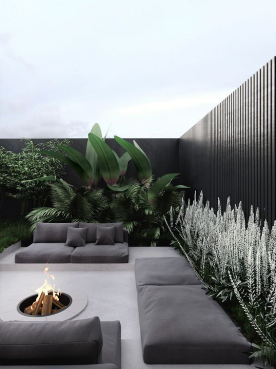 minimalistische Terrassengestaltung verschiedene Graunuancen schwarze Wand Sitzmöbel Feuerstelle viele grüne Pflanzen ringsum