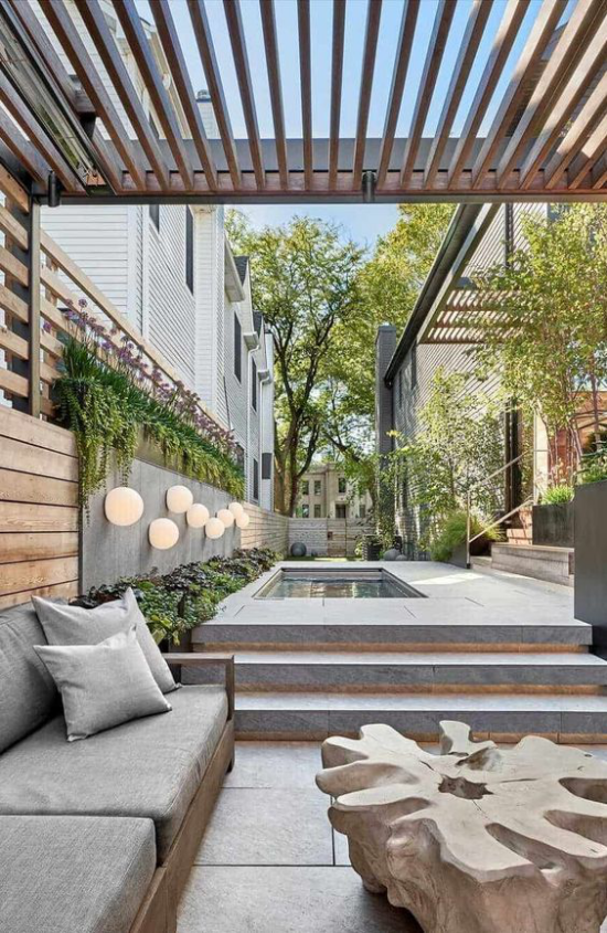 minimalistische Terrassengestaltung Überdach Sitzbank graue Sitzkissen Treppen Pool grüne Pflanzen runde Lampen