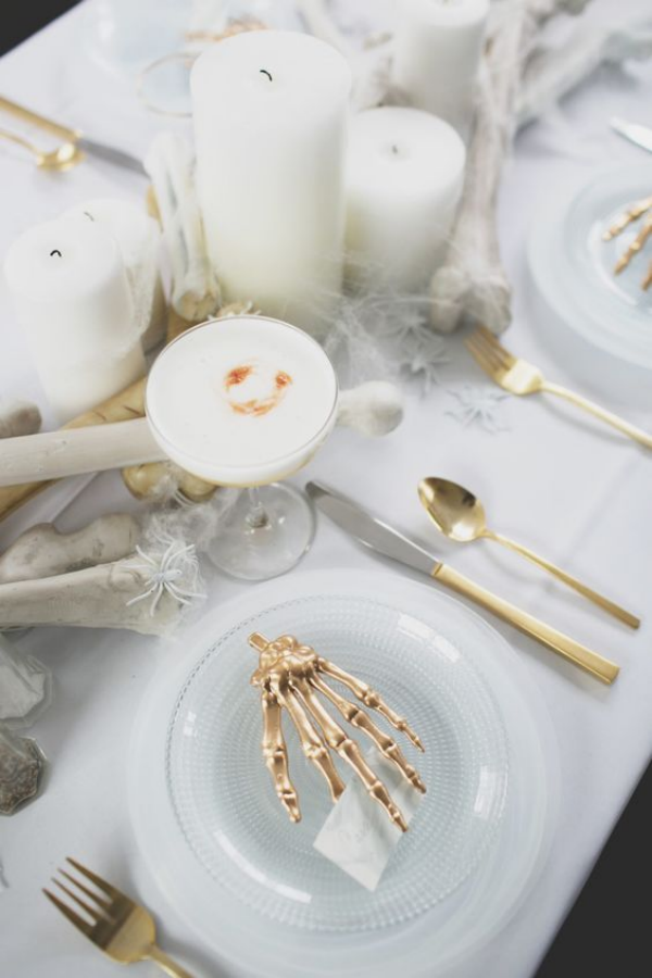Weiße Halloween Deko Ideen festlich gedeckter Tisch weißer Schmuck Hand in goldgelb auf einem weißen Teller weiße Kerzen