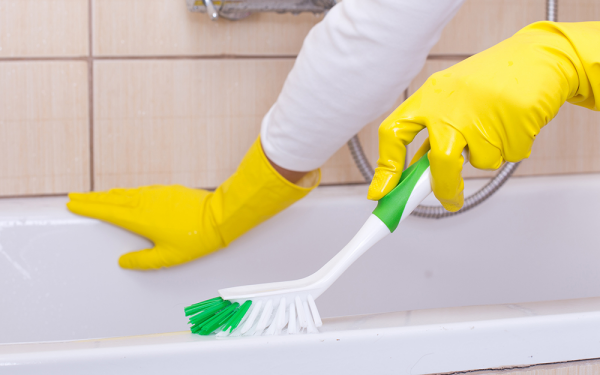 Badewanne reinigen clevere Tipps für strahlenden Glanz Frau gelbe Schutzhandschuhe tragen mit Bürste die Wanne putzen