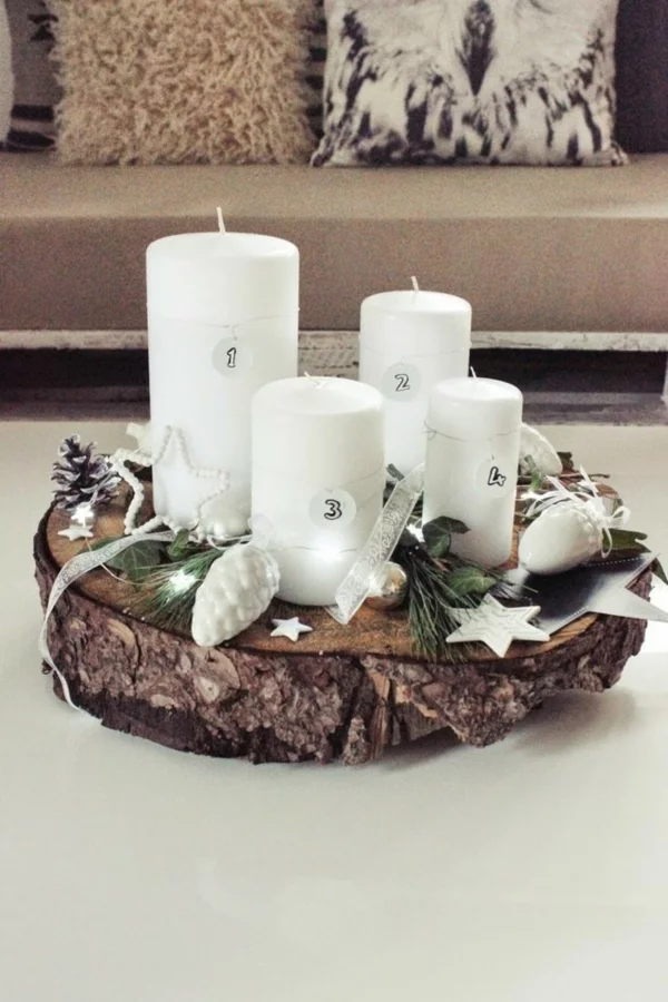 rustikaler Adventskranz mit weißen Stumpemkerzen und dekorativen Zapfen und Sternen auf einer Holzscheibe