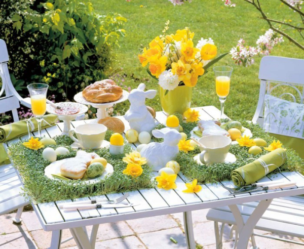 Osterdeko für draußen festlich dekorierter Tisch im Freien bunte Eier gelbe Narzissen viel Grün