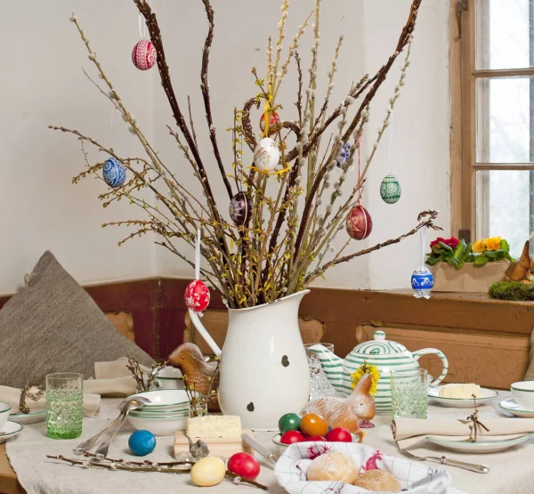 Tischdeko zu Ostern  blühende Zweige in einer alten Gießkanne mit bunten Eiern geschmückt rustikaler Look
