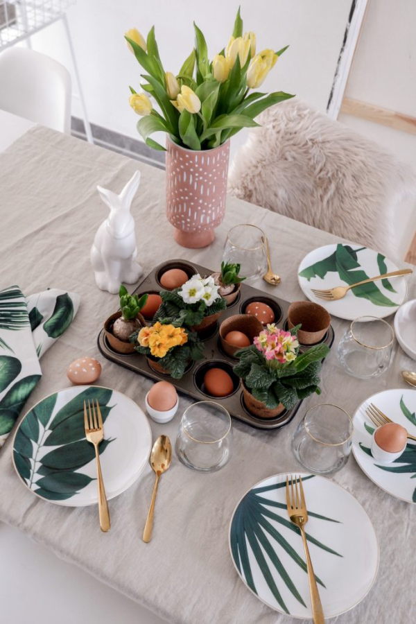 Tischdeko zu Ostern festlich gedeckter Tisch Vase mit Tulpen im Zentrum Frühlingsblumen in kleinen Töpfen Hasen Eier