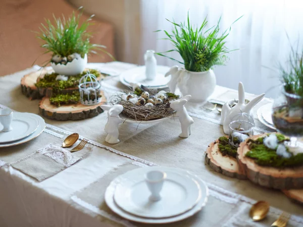 Tischdeko zu Ostern stilvoller Schmuck kleine weiße Hasen aus Porzellan Holzscheiben Moos Gras