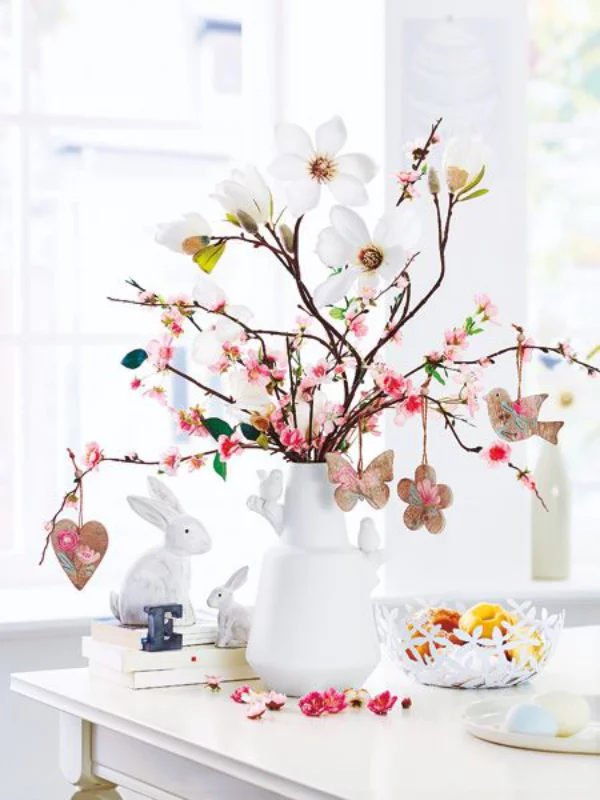 Tischdeko zu Ostern weiße Vase blühende Kirschzweige selbstgebastelte Herzen Schmetterlinge Blumen Vögel aufhängen Blickfang