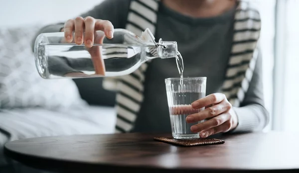 Close up of young Asian woman pouring water from bottle into the glass on a coffee table at home. Healthy lifestyle and stay hydrated
