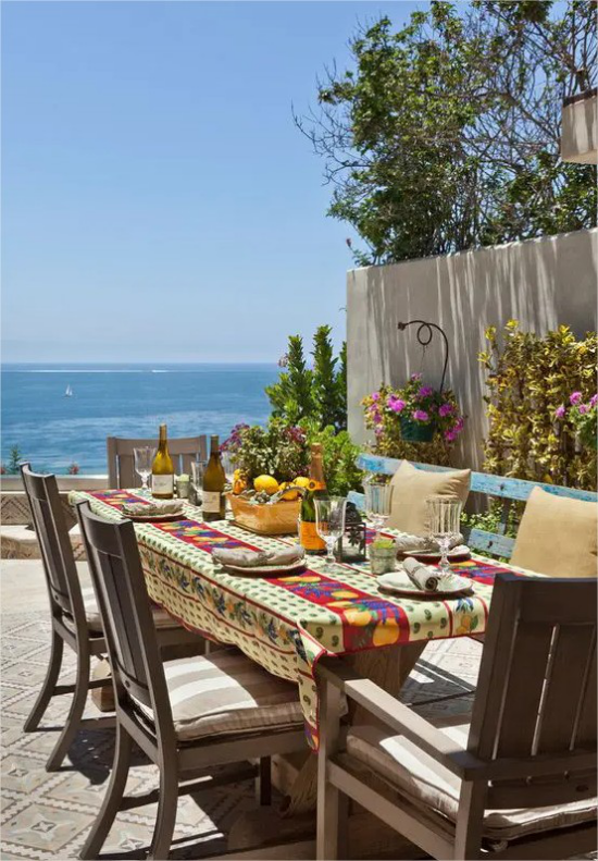 mediterraner Außenbereich Esstisch auf der Terrasse Holzstühle bunte Tischdecke Azurblau des Meeres