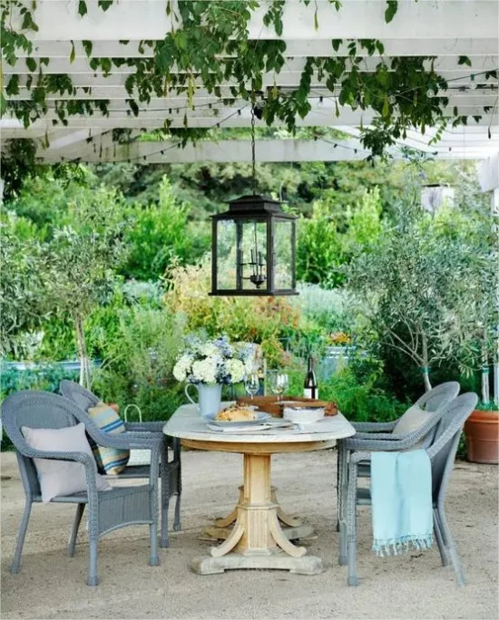 mediterraner Außenbereich Sitzecke unter Vordach aus Holz viel Grün im Hintergrund Kletterpflanzen Hängeleuchte