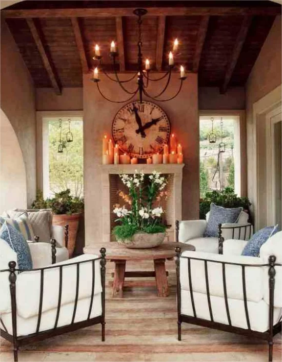mediterraner Außenbereich glamourös gemütlich Sessel aus Schmiedeeisen weiße Sitzkissen Kamin Kerzen kleiner Holztisch Pflanzgefäß aus Stein