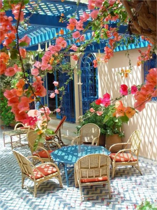 mediterraner Außenbereich niedriger runder Tisch Korbsessel schöne Kletterpflanzen farbenfroh einladend gemütlich