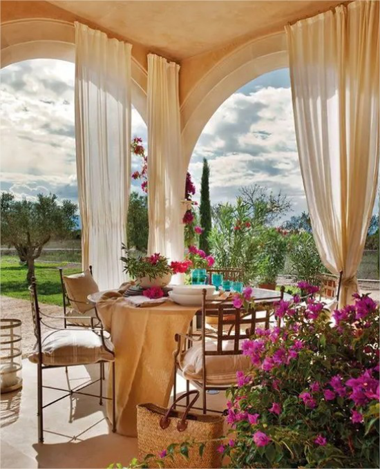 mediterraner Außenbereich perfekte Pergola im Mittelmeerstil Vorhänge aus leichtem durchsichtigem Stoff Sitzgarnitur viele Blumen Naturverbundenheit