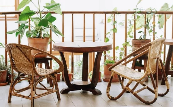 aktuelle Gartentrends runder Holztisch zwei Korbstühle auf dem Balkon mit grünen Topfpflanzen kombinieren gemütlichen Außenbereich gestalten 