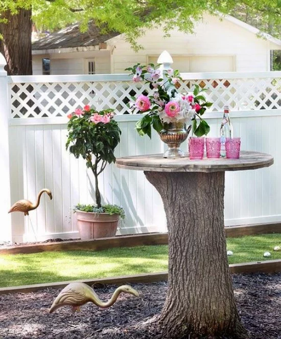 Baumstamm als Gartendeko hoher Baumstumpf Holzplatte als Tisch darauf Blumen Getränke schöner Anblick