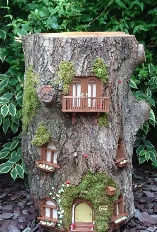 Baumstamm als Gartendeko kleines Haus mit Fenstern Fantasiewelt der Kinder Moos grünes Laub