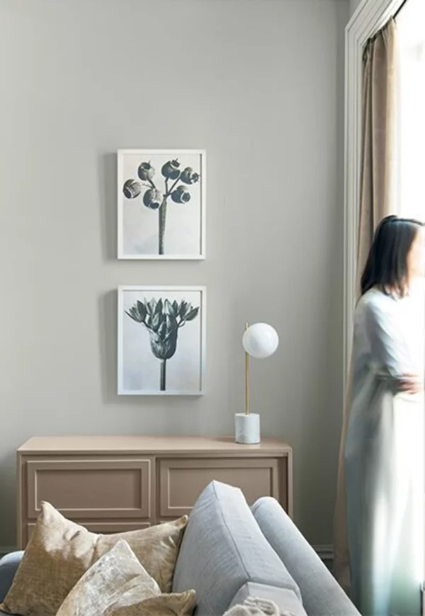 Dominierende Sommerfarben Wohnzimmer Frau am Fenster warmes Grau an der Wand helles Beige Sofa