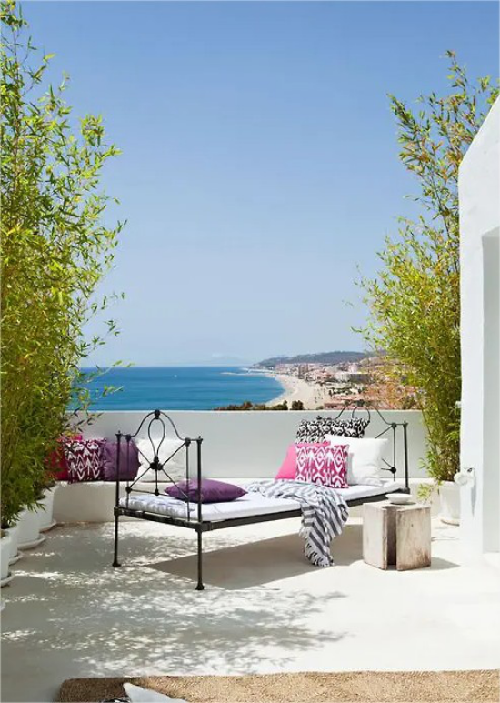 Feminine Outdoor-Bereiche offene Veranda im mediterranen Stil Weiß dominiert Metallbett bunte Kissen herrlicher Blick auf Meer
