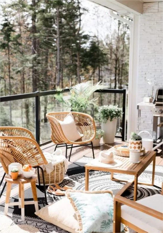 Gestaltungsideen fuer Balkon Moebel aus Holz Korbsessel Kissen Teppich gruene Pflanzen herrlicher Blick zum Wald