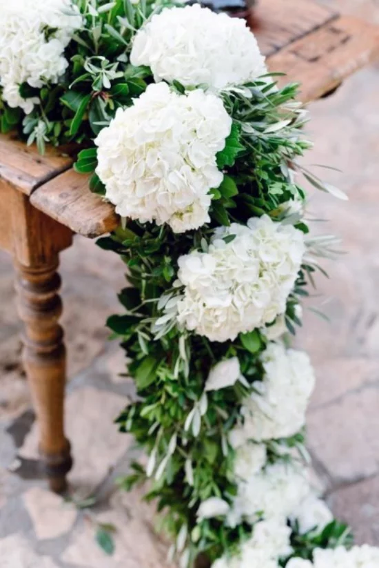 Hochzeitsdeko mit Hortensien weiße Blueten gruene Blaetter großartige Girlande auf dem Tisch