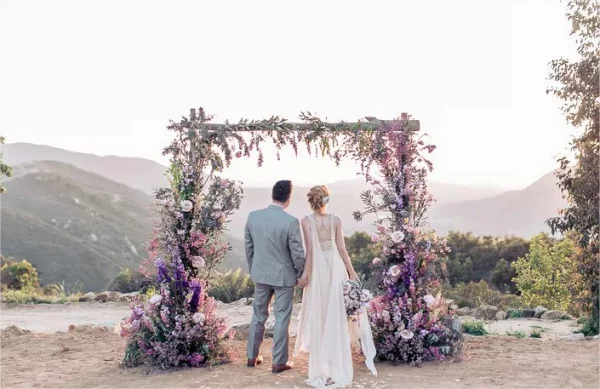 Hochzeitsdeko mit Lavendel Brautpaar vor einem ueppig geschmueckten Bogen Altar