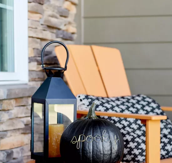 Herbstdeko mit Kuerbissen ruhige Sitzecke auf Veranda Sessel Laterne schwarzer Kuerbis