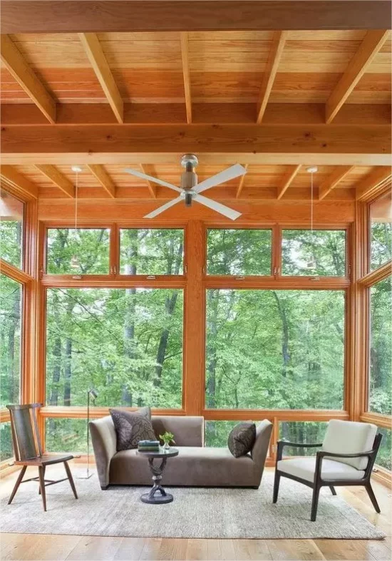 Moderne Glasveranda Holzdecke elegantes Sofa graue Kissen deckenhohe Fenster herrlicher Blick draußen viel Gruen