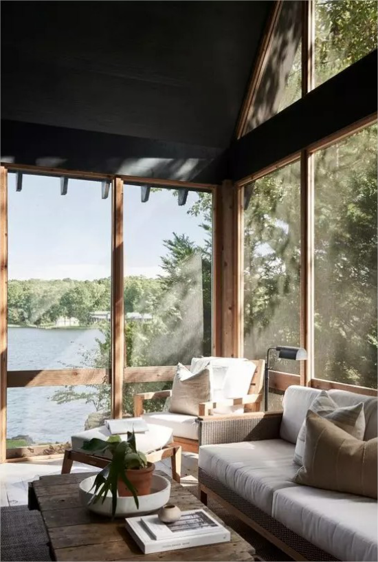 Moderne Glasveranda weiße Moebelbezüge viel Sonnenlicht Sofa Sessel Hocker See draußen