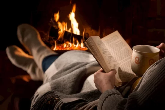 Heizen mit Brennholz warm angezogen Wolldecke vor dem Kamin Buch Teetasse in der Hand