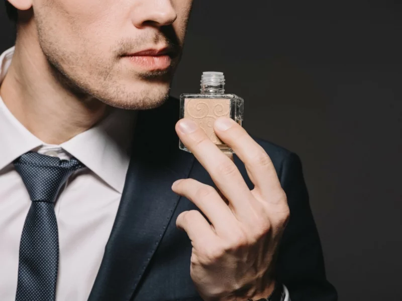 Mann mit Anzug riecht an einem Parfum 