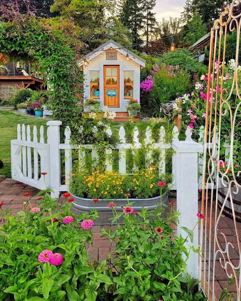 nachhaltig gärtnern - kleines Gartenhaus mit weißem Zaun aus Holz 
