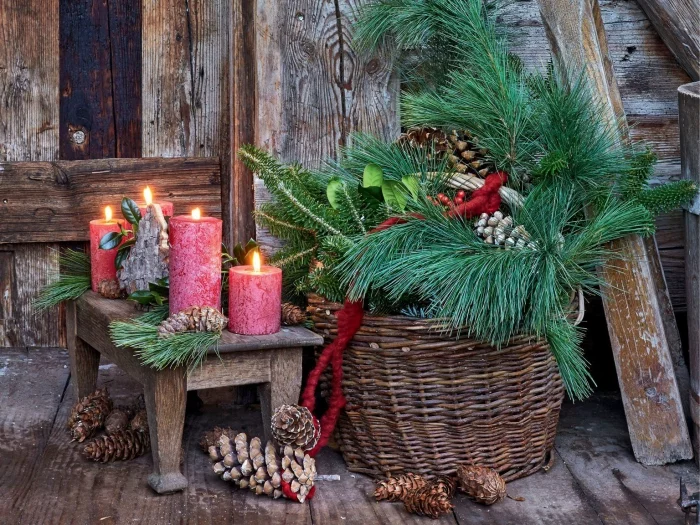 Den Außenbereich weihnachtlich dekorieren Korb mit Tannengrün daneben vier rote Stumpenkerzen