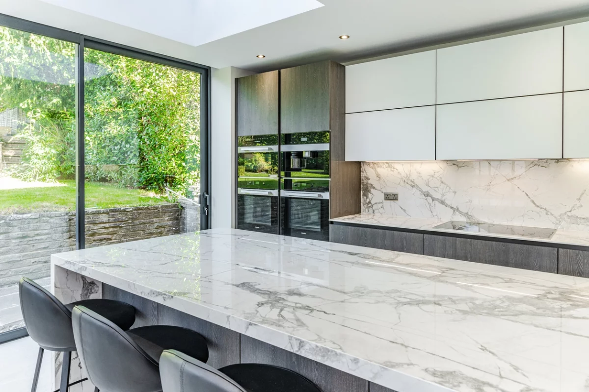 Moderne offene Küche mit Kücheninsel aus Marmor und mit Blick zum Garten