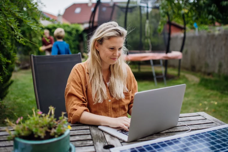 Sitzecke im Garten – junge Frau arbeitet am Laptop im Freien