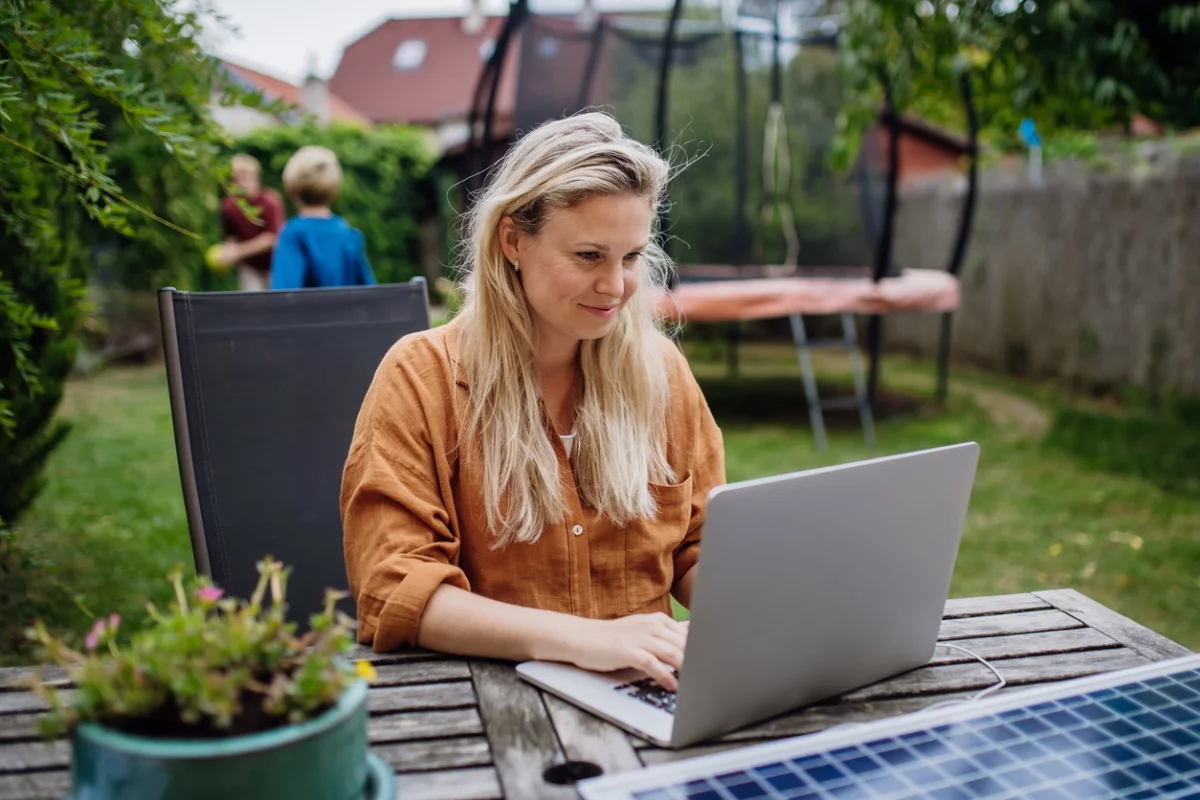 Sitzecke im Garten – junge Frau arbeitet am Laptop im Freien