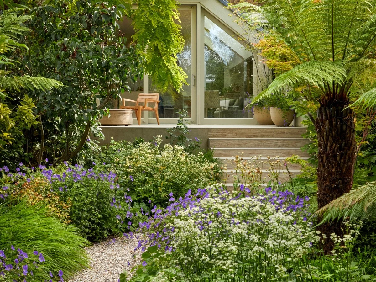 ein Naturgarten mit üppigen Pflanzen und Gartenweg mit Kies belegt