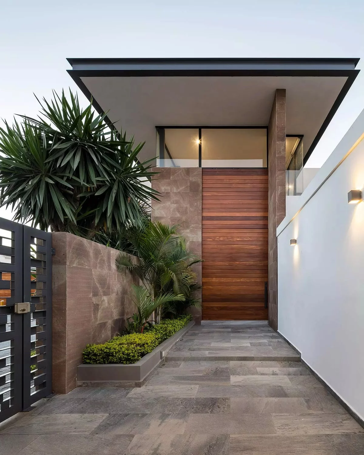 schöner moderner Hauseingang mit Haustür aus Holz und grünen Pflanzen links