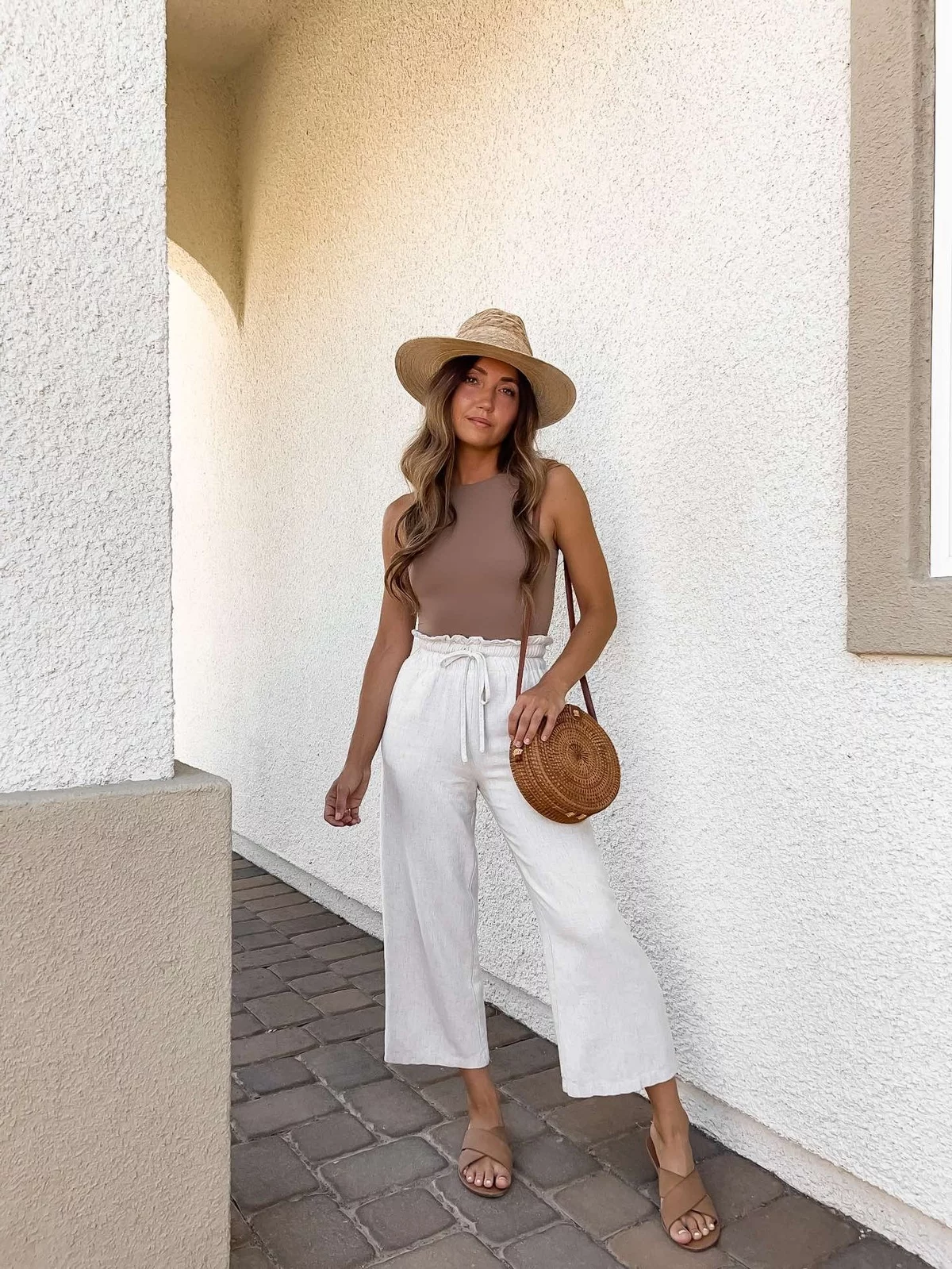 weiße Leinenhose kombiniert diese junge Frau mit braunem Oberteil und Tasche