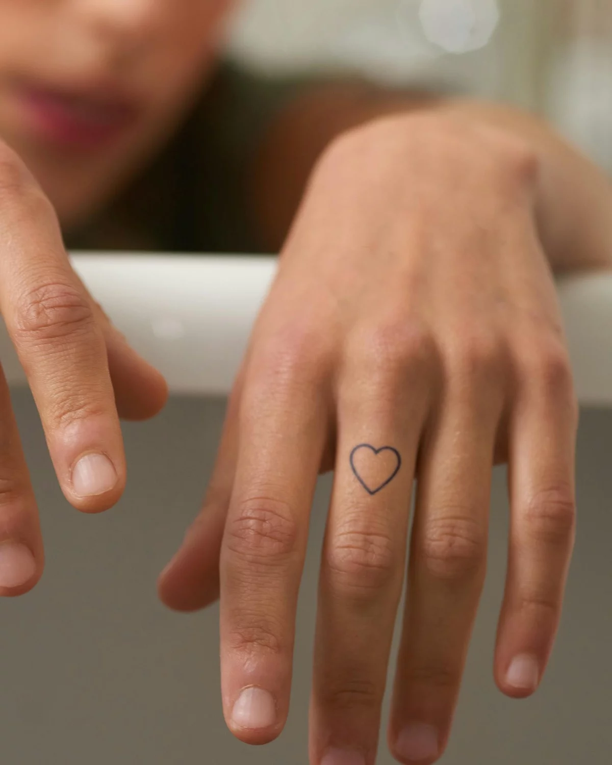 minimalistisches Herz Tattoo am Mittelfinger der linken Hand