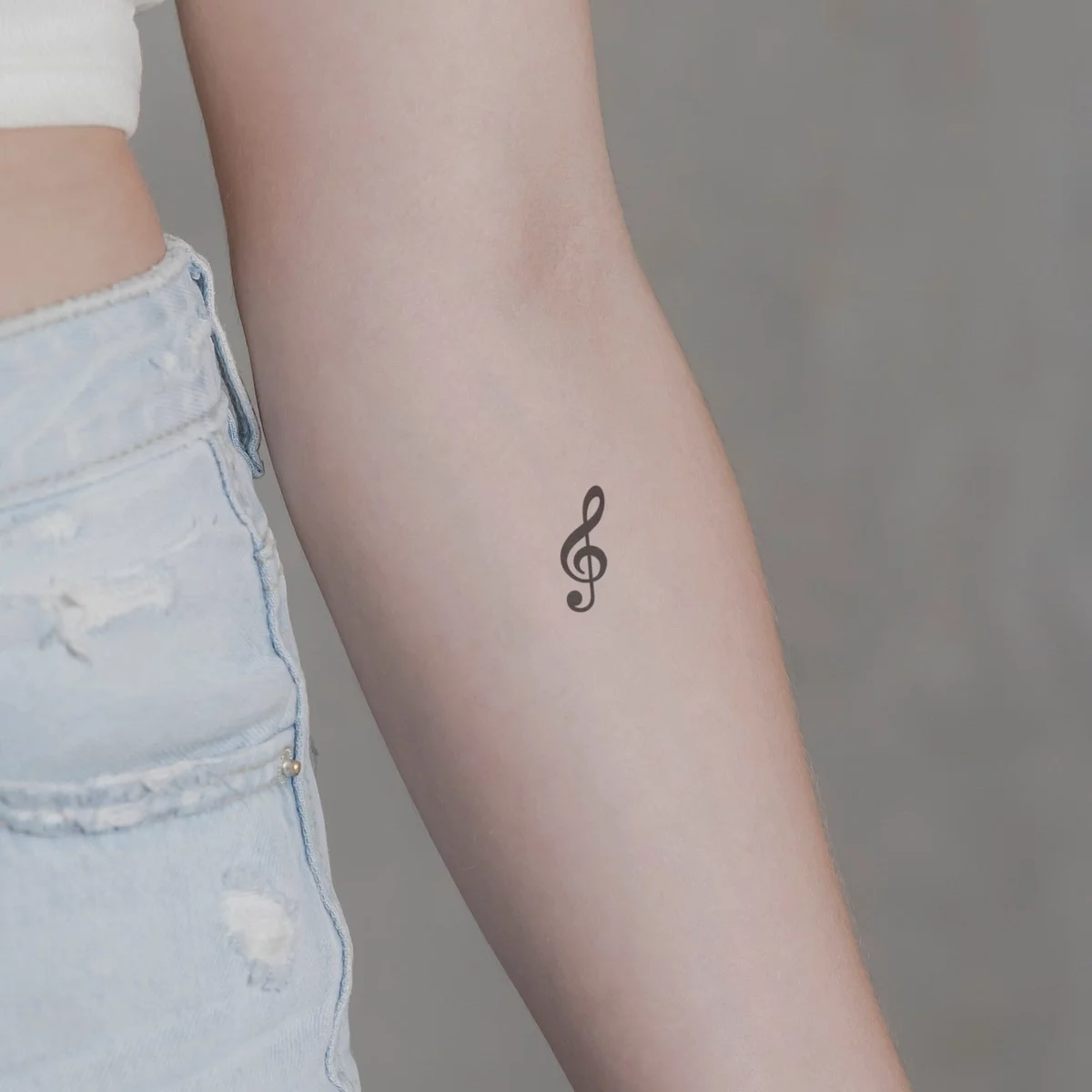 Notenschlüssel als minimalistisches Tattoo am Unterarm