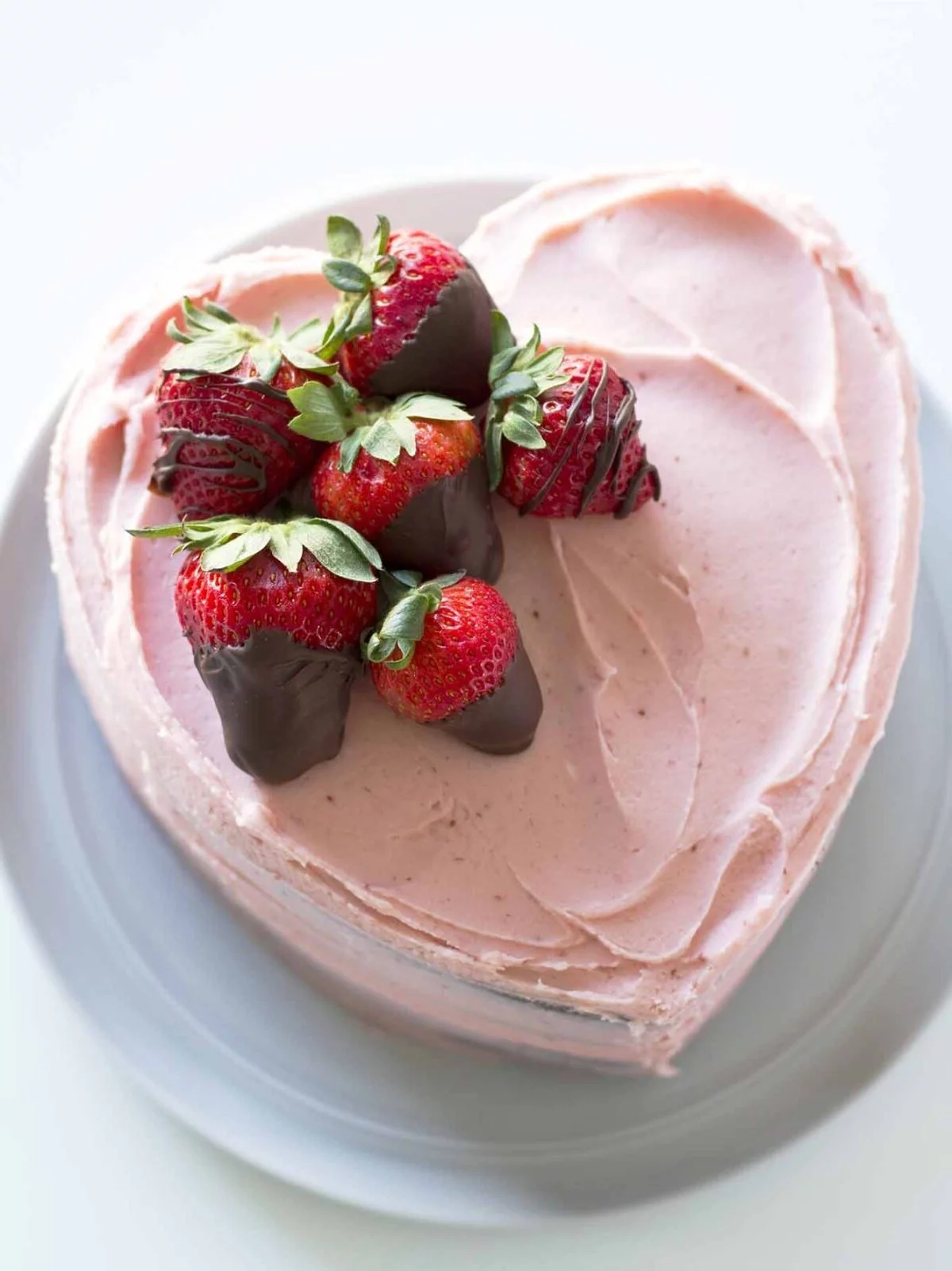 Erdbeerkuchen in Herzform mit rosa Creme und Früchte mit Schokolade dekoriert