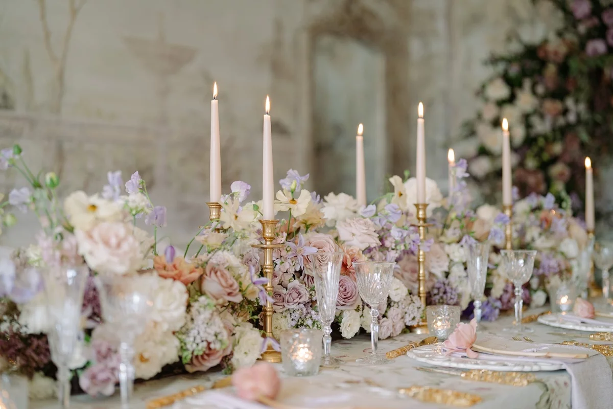 Blumen in zarten Farben und weiße Kerzen schmücken den Hochzeitstisch