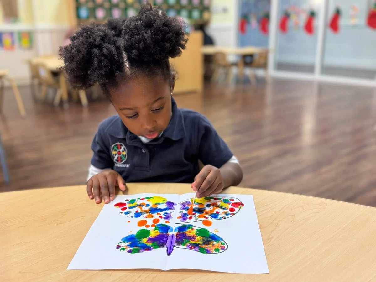kleines Mädchen malt einen Schmettering im Kindergarten 