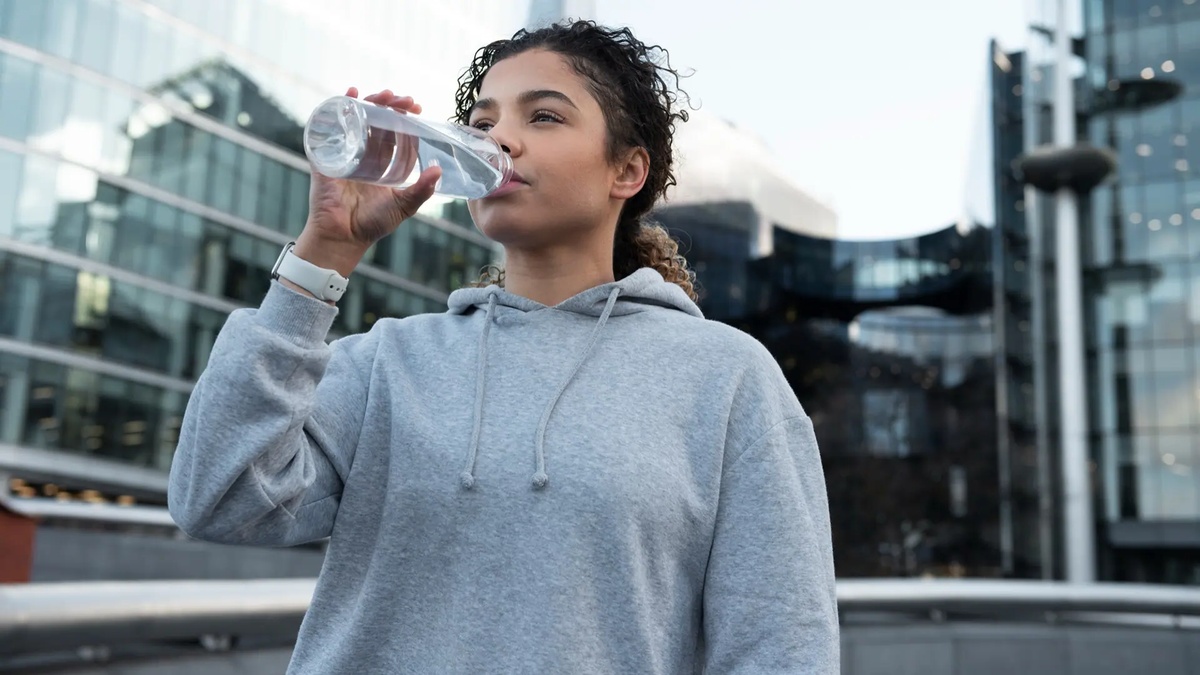 Junge Sportlerin trinkt Wasser nach Training