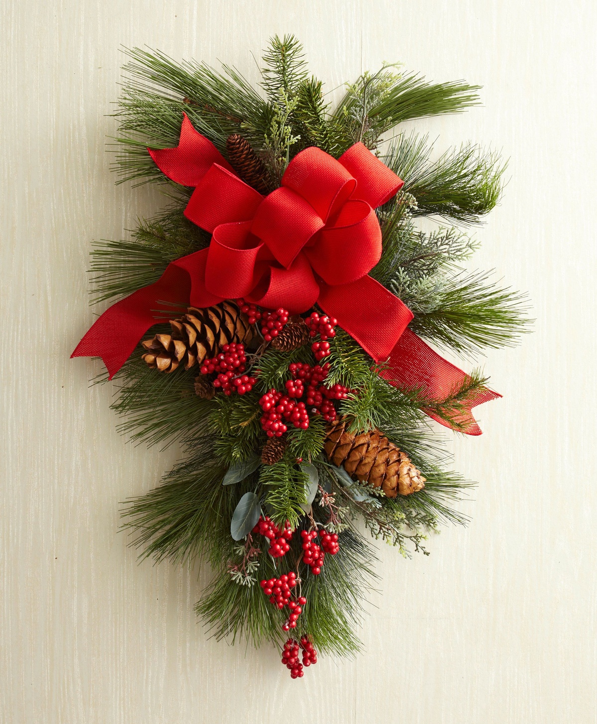 ein Türkranz in länglicher Form mit roter Schleife, zapfen und roten Stechpalmenbeeren 