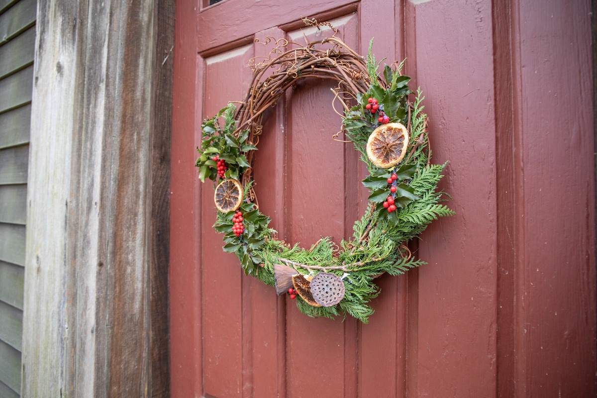 untere Hälfte des Kranzes dekorieren mit grünen Zweigen, Zitrusscheiben, Stechpalmenbeeren usw